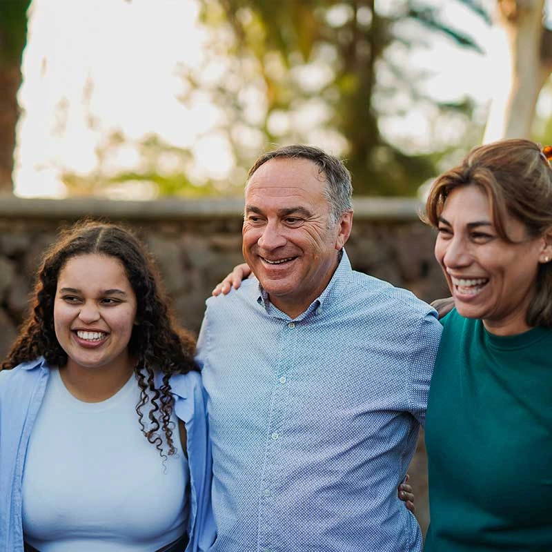 Drei Menschen stehen eng beisammen und lachen, sie wirken verbunden und fröhlich.